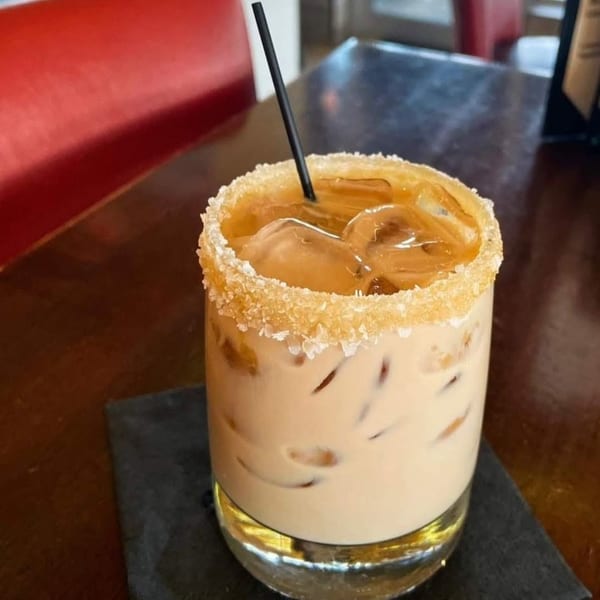 Iced coffee cocktail with a sugared rim and black straw on a dark table with a red booth.