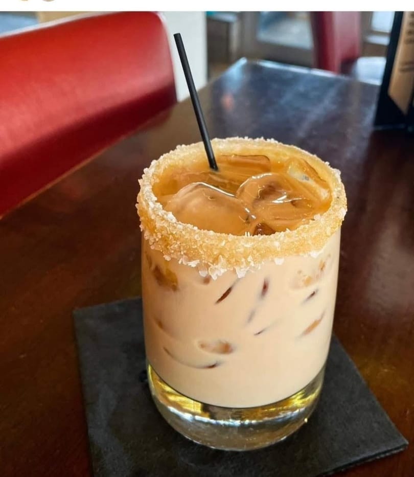 Iced coffee cocktail with a sugared rim and black straw on a dark table with a red booth.
