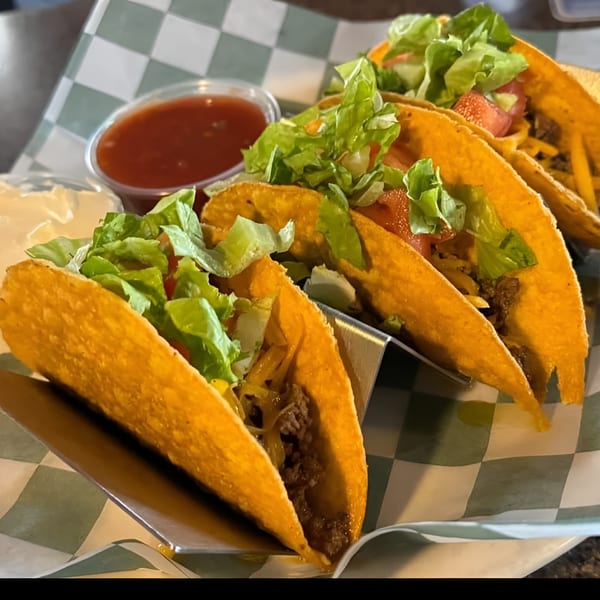 Four crispy tacos filled with ground beef, cheese, lettuce, and tomato, with salsa and sour cream.