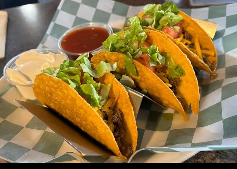 Four crispy tacos filled with ground beef, cheese, lettuce, and tomato, with salsa and sour cream.