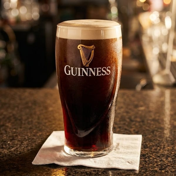 A pint of Guinness beer with a creamy head sits on a napkin on a dark bar.